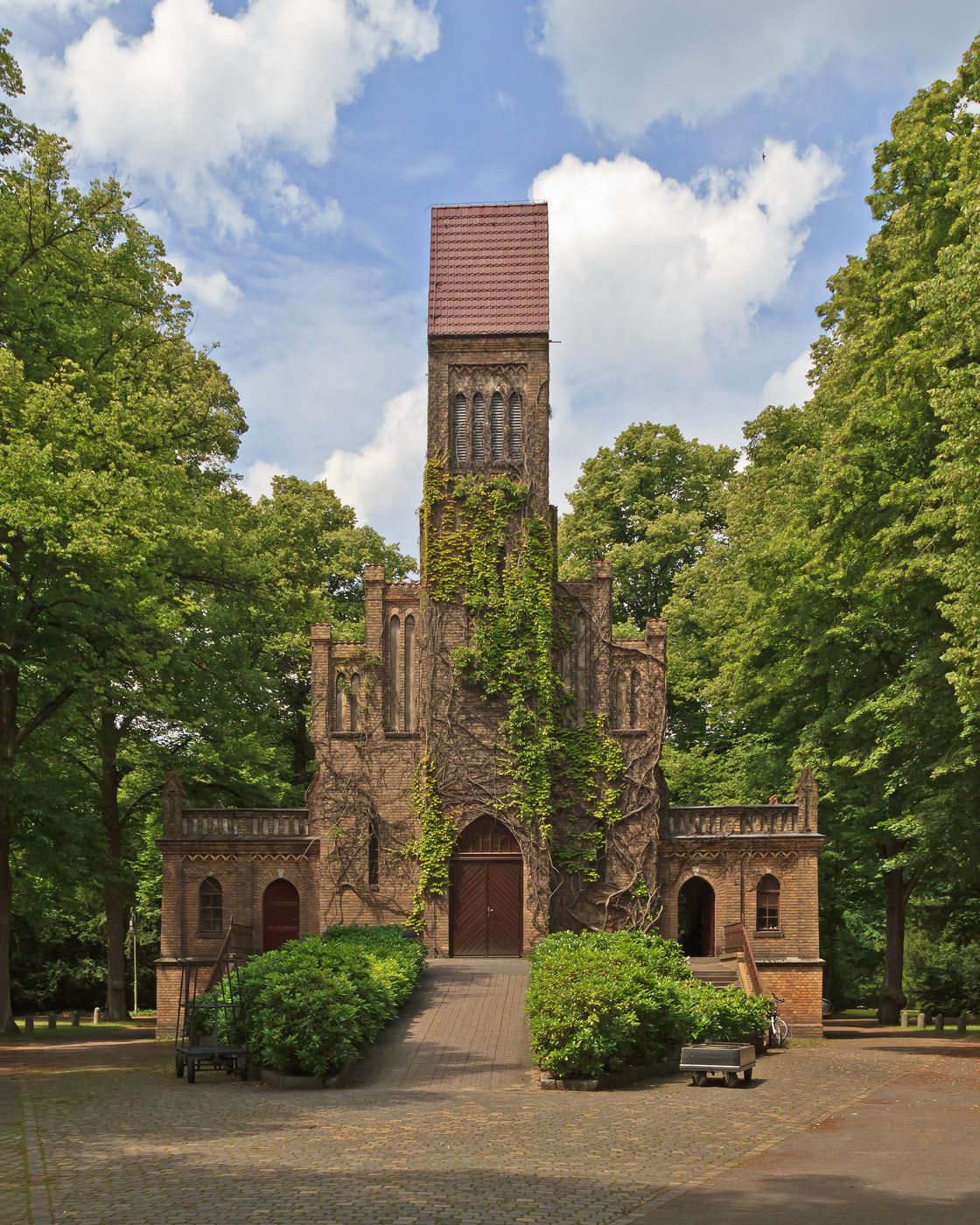 Brick chapel with a tall tower among dense mature trees at In den Kisseln Cemetery